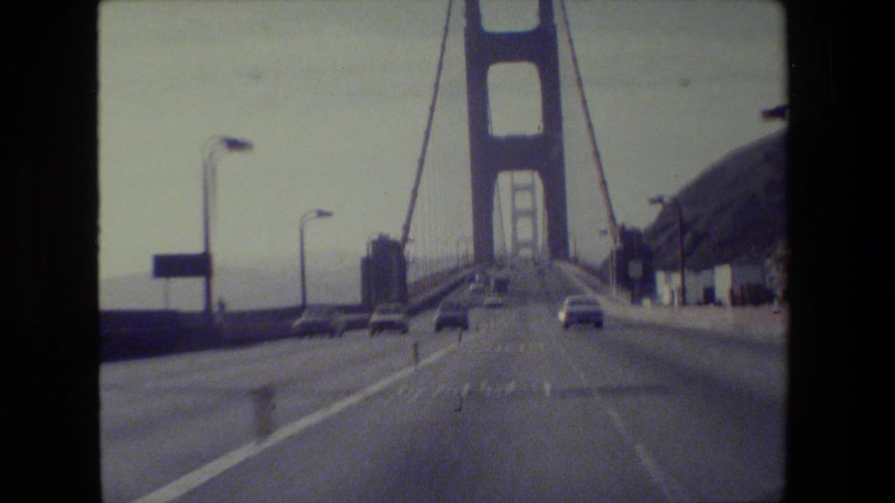 Driver’s-eye view approaching a Golden Gate Bridge tower with cars ahead on the roadway.