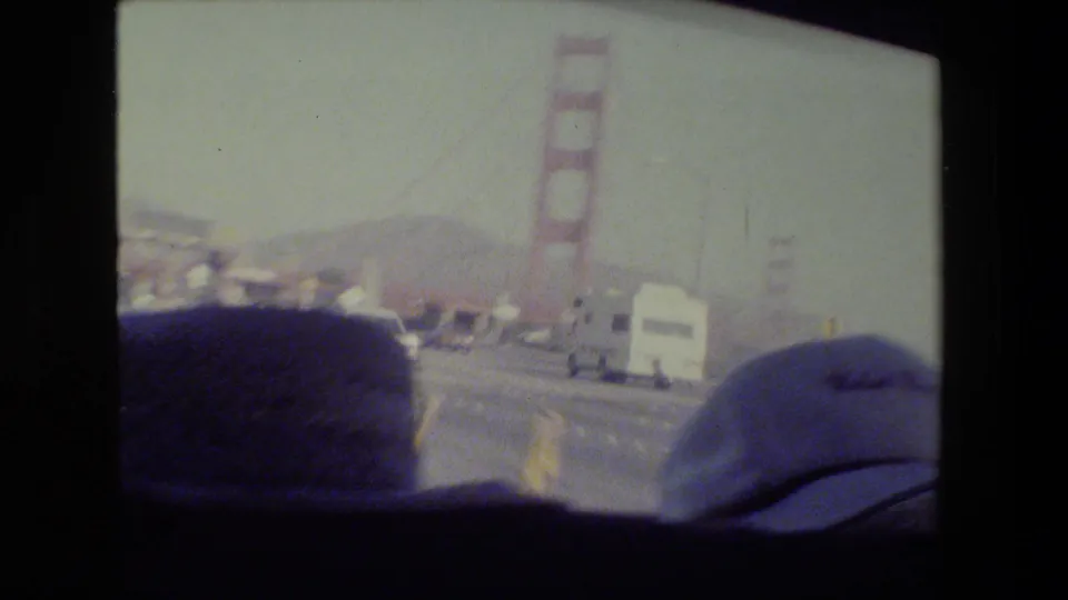 1984 San Francisco bridge-driving footage showing the Golden Gate Bridge tower, roadway traffic, and parts of the filming vehicle in the foreground.