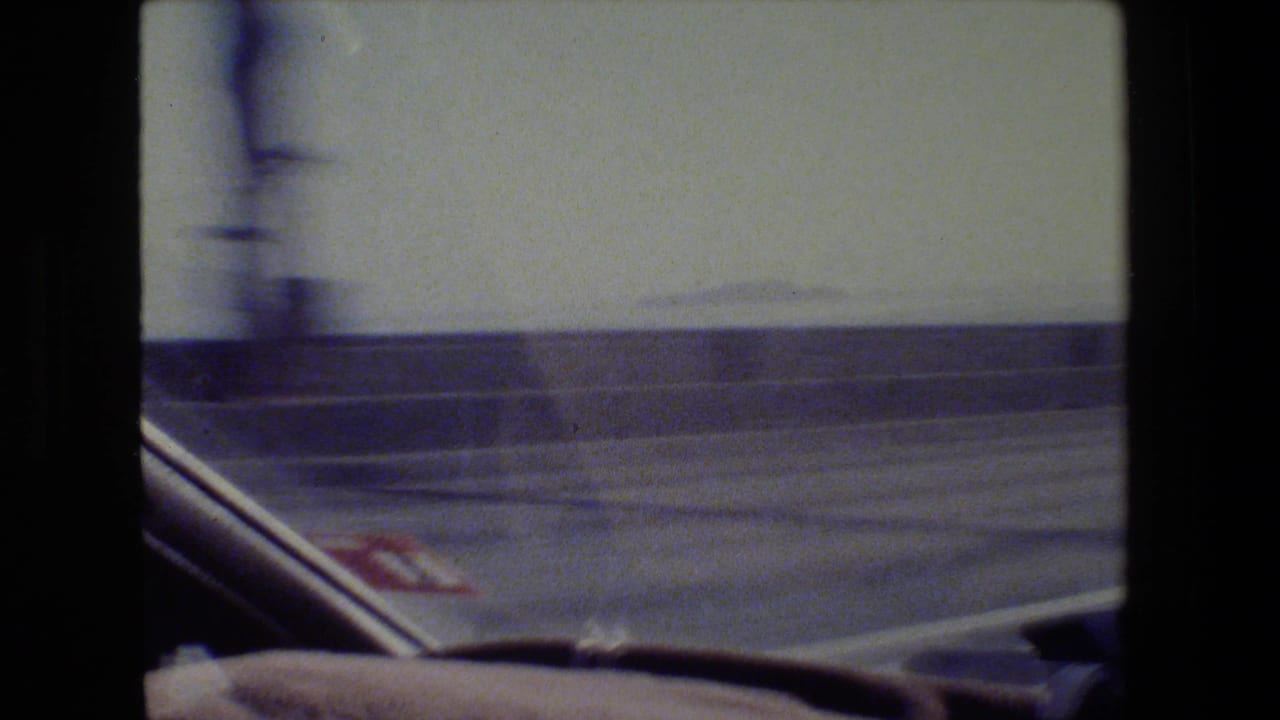 Moving vehicle view past a concrete barrier with a car window edge and pale sky.