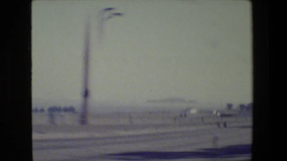 1984 San Francisco-area 8mm frame with a tall street lamp, hazy roadway, distant low forms, and visible film softness.