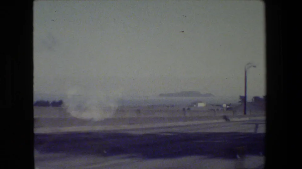 Motion-blurred 1984 San Francisco-area roadway frame with a street lamp, barrier, open sky, and distant roadside forms.