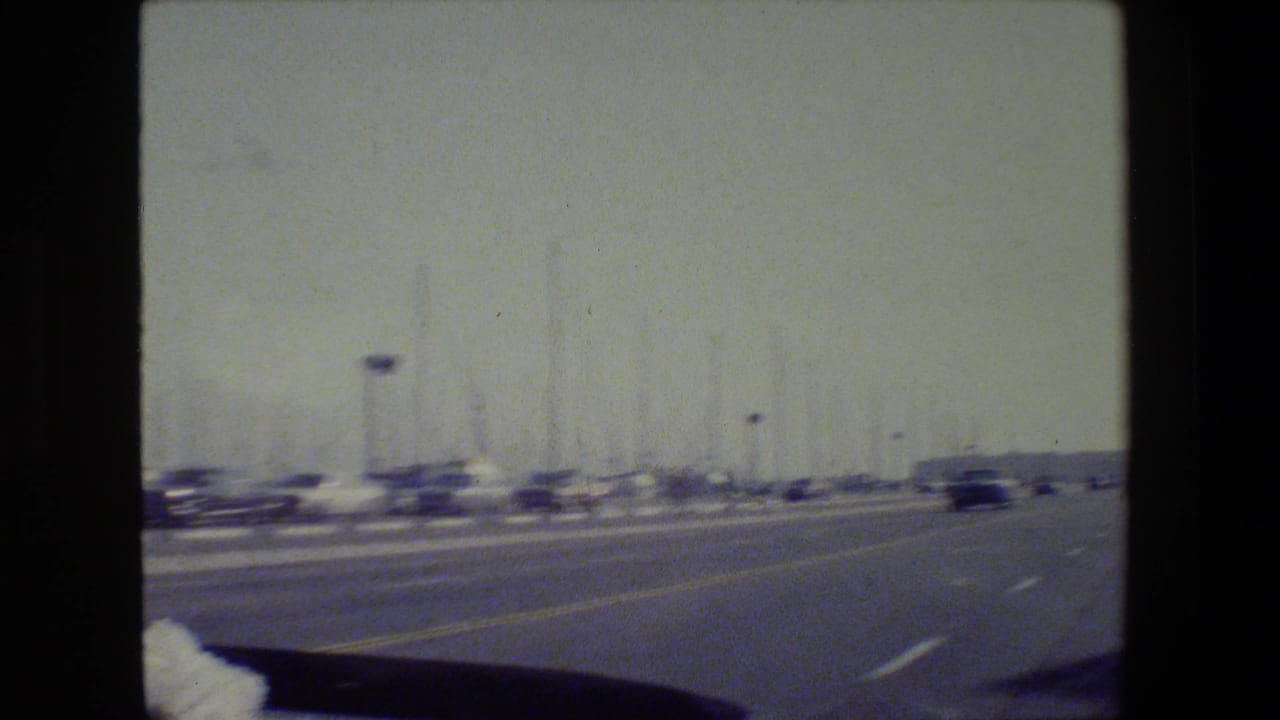 1984 San Francisco home-movie view from a moving vehicle, showing a road near marina masts under hazy light.