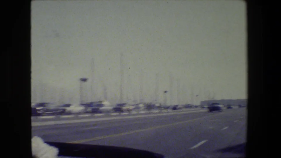 1984 San Francisco home-movie view from a moving vehicle, showing a road near marina masts under hazy light.