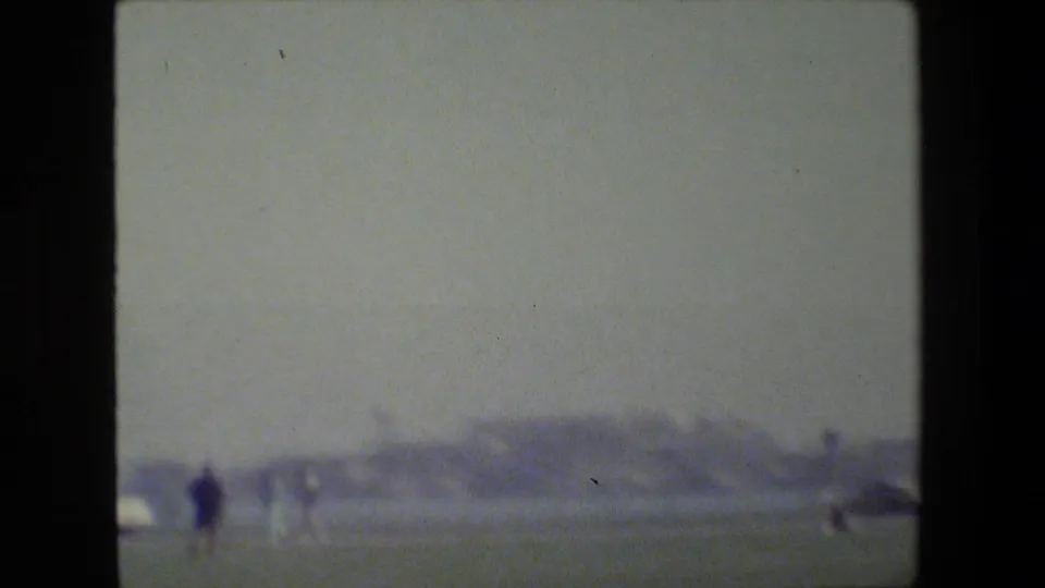 San Francisco 1984 home-movie frame showing distant small figures on open grass near a hazy waterfront landscape.