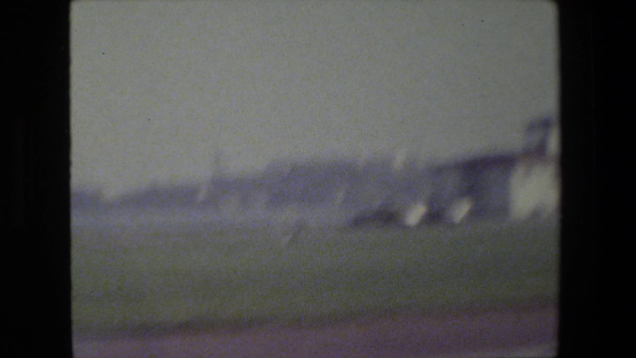Blurred roadside view with pale sky and dark film-frame edges.