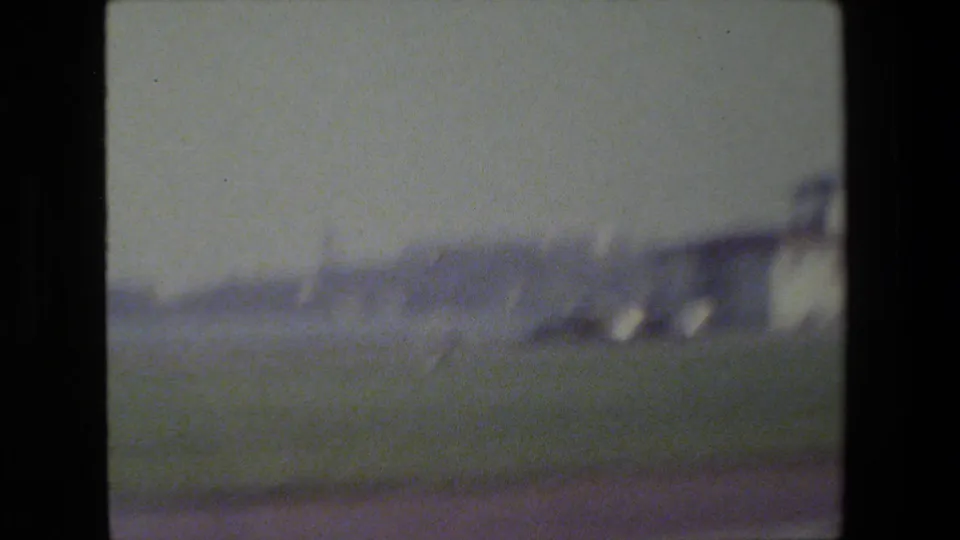 Soft, motion-blurred 8mm frame from a moving view in San Francisco, with indistinct roadside structures under a hazy sky.