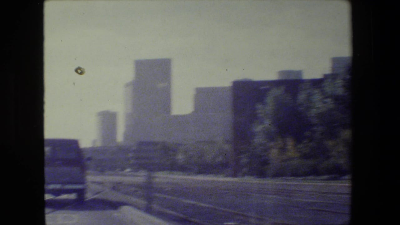 Downtown skyline beyond a road with a van and roadside railings.