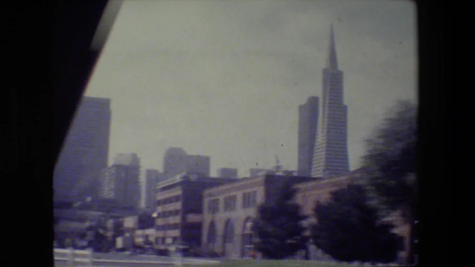 San Francisco view with the Transamerica Pyramid rising behind lower buildings, trees, and street details in faded 8mm color.