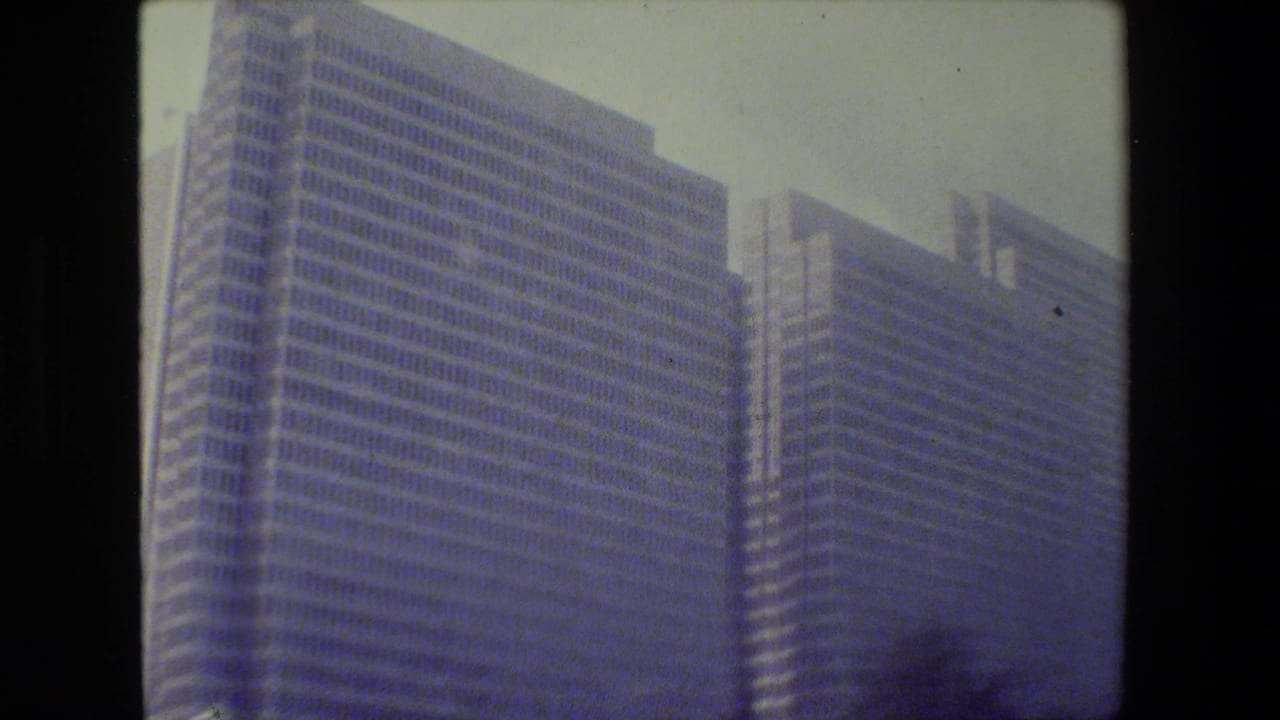 1984 San Francisco home-movie frame showing tall glass office buildings, softened by motion blur and blue color fading.