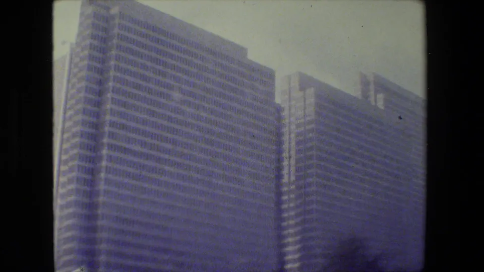 1984 San Francisco home-movie frame showing tall glass office buildings, softened by motion blur and blue color fading.