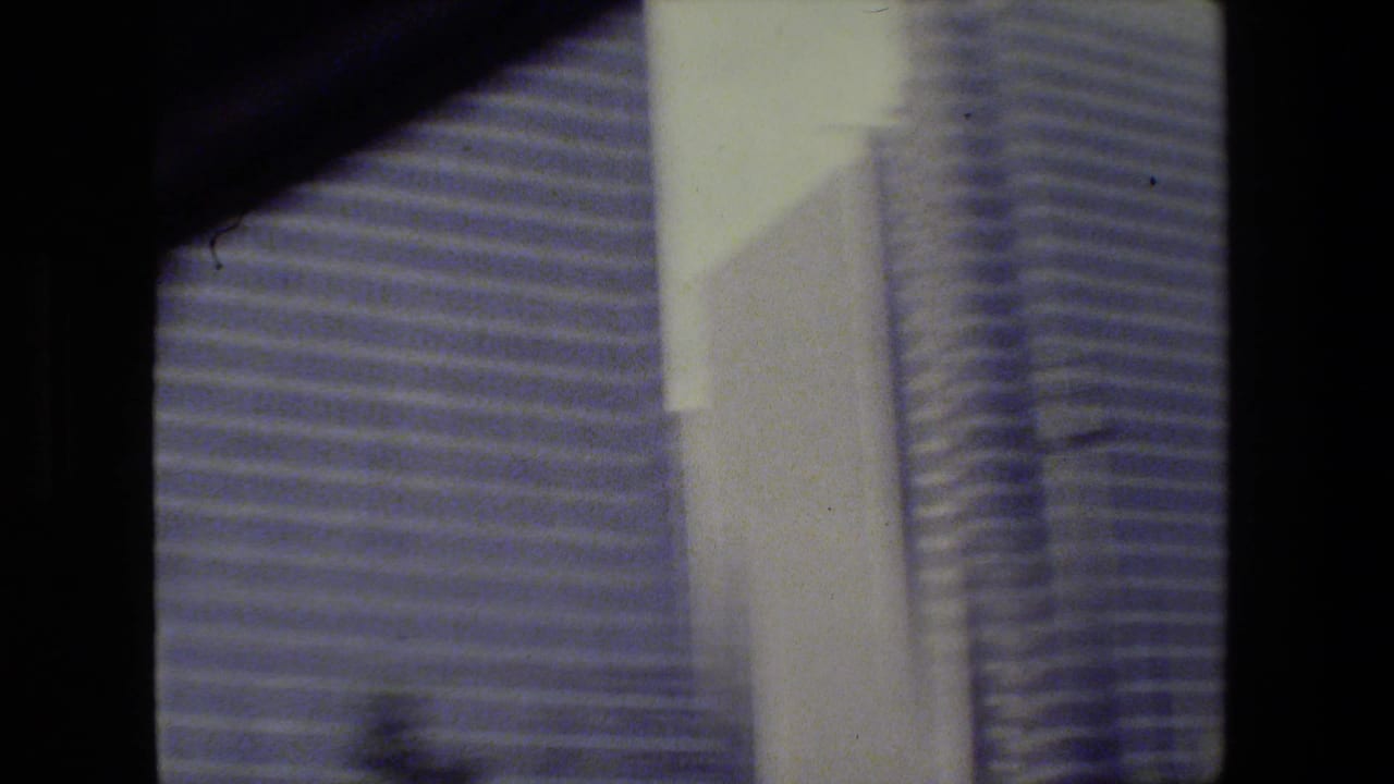 Blurred tall buildings seen through a dark vertical window or film edge.