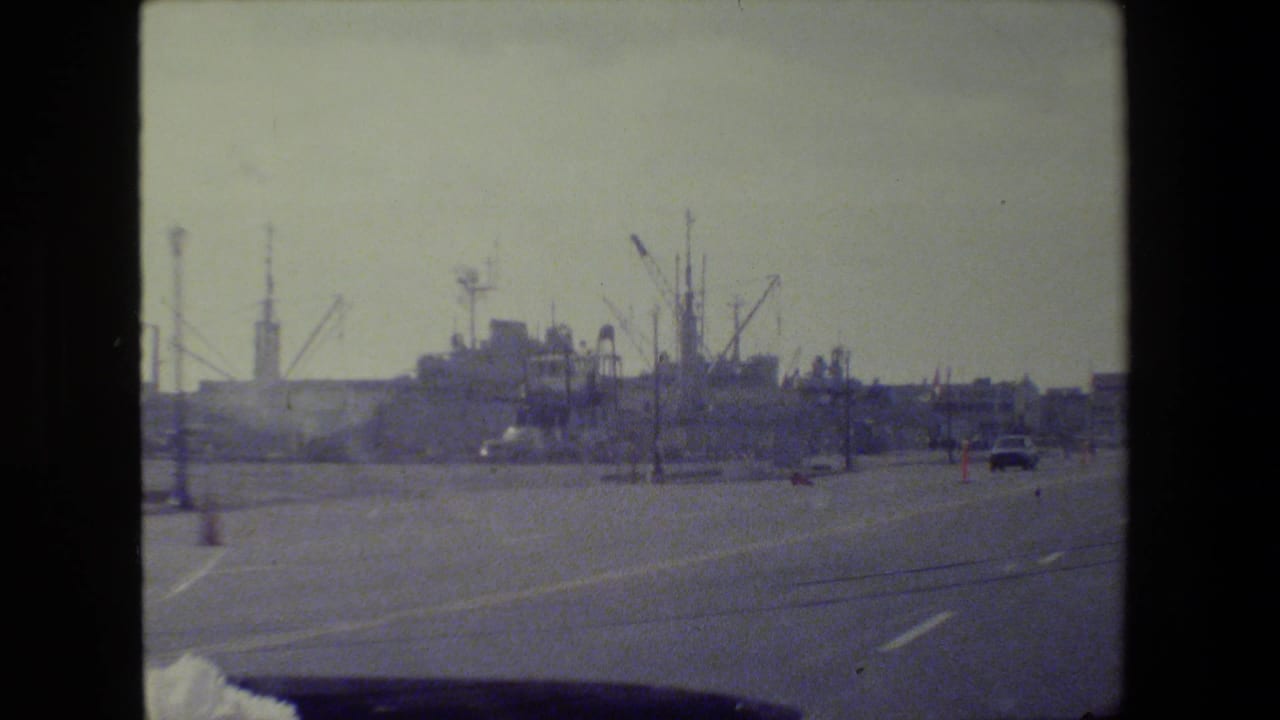 Forward road view with distant cranes, light poles, and vehicles.