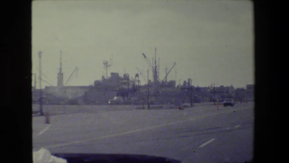 Driver-view frame on a San Francisco roadway with industrial cranes, light poles, and traffic ahead in soft 8mm focus.