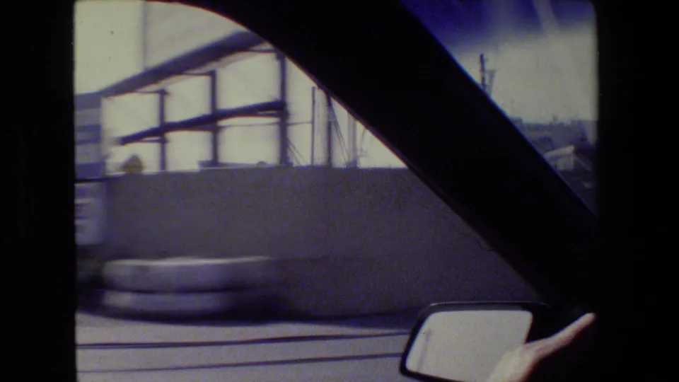 San Francisco driving frame with motion-blurred roadside barrier, car window frame, mirror, and part of the dashboard flower.