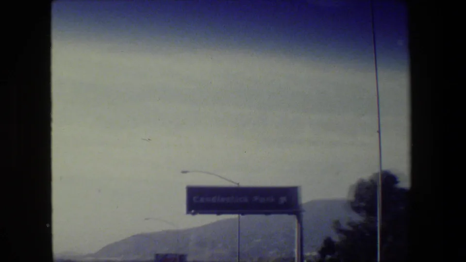 San Francisco-area 8mm frame with a visible Candlestick Park freeway sign, distant hills, and roadside light poles.