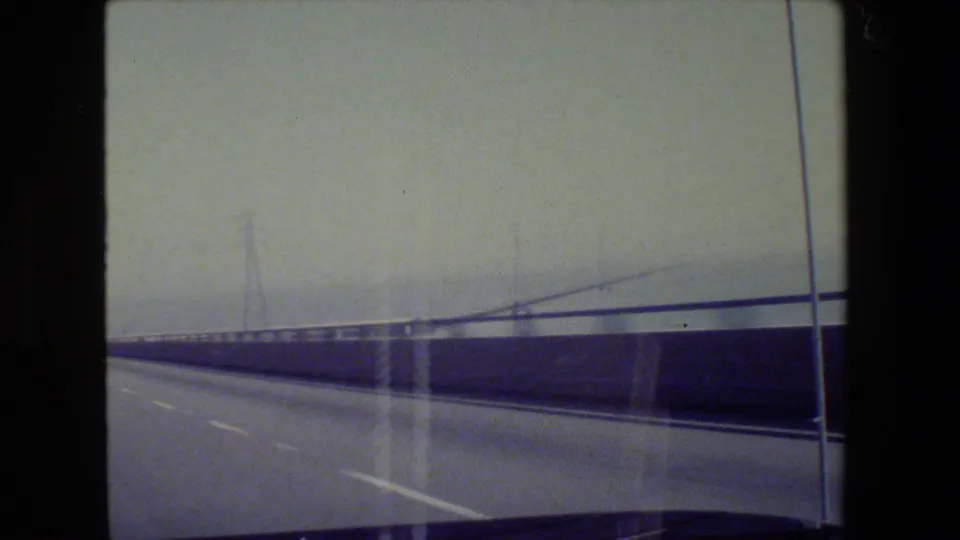1984 California road-trip frame showing a bridge or elevated highway with railings, light poles, and power towers.