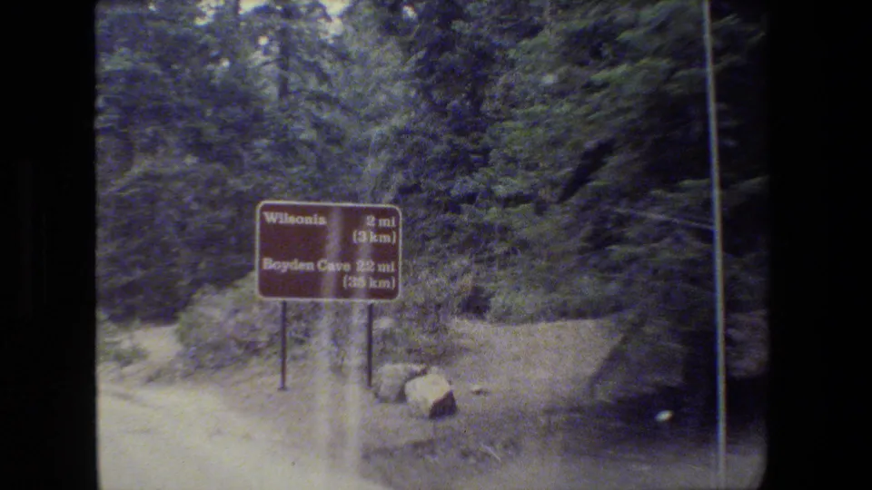A roadside sign near wooded terrain points toward Wilhonia and Boyden Cave, filmed in 1984 from a moving vehicle.