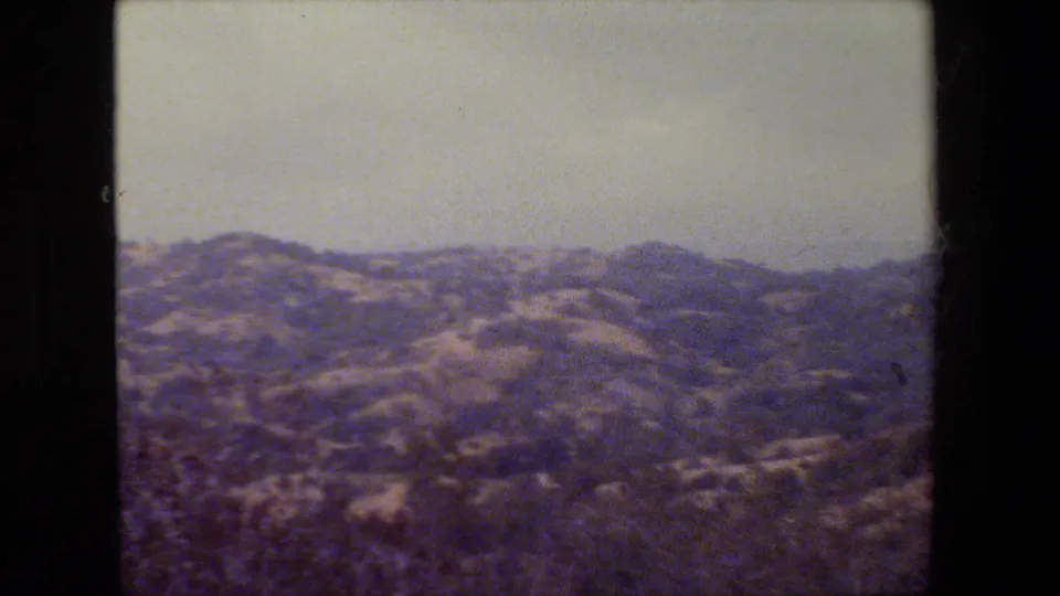 Faded 8mm frame of low California hills with scrub vegetation and a bright washed-out sky.