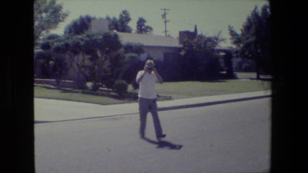 Older man raises a camera toward his face in a residential street.