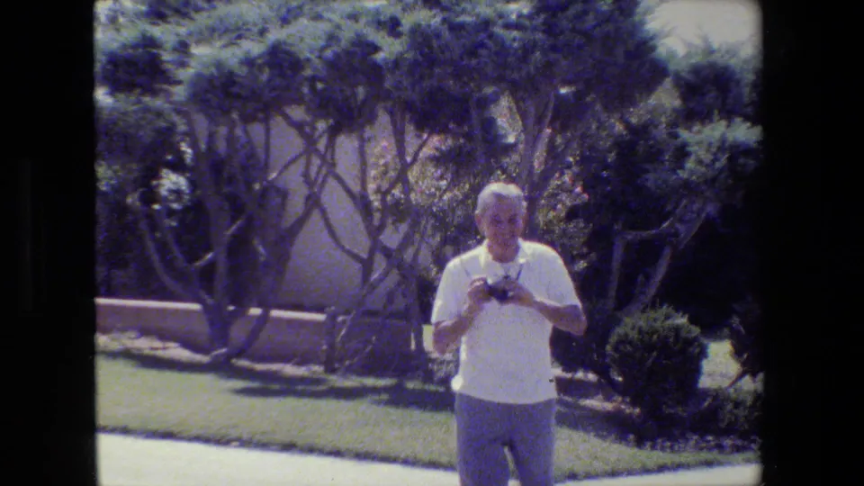 At the end of the clip, the older man lowers his camera near a manicured lawn and trees in the San Francisco residential setting.