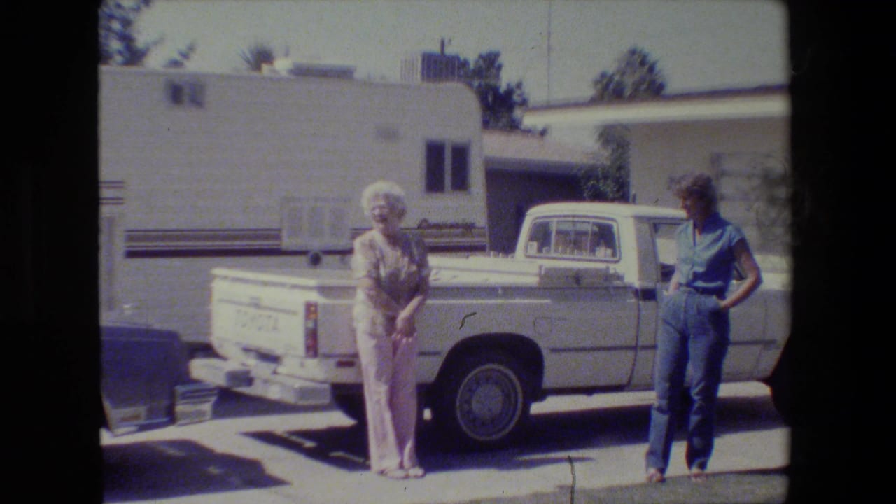 In 1984 San Francisco home-movie footage, two older women stand near a white Toyota pickup with a light-colored building behind them.