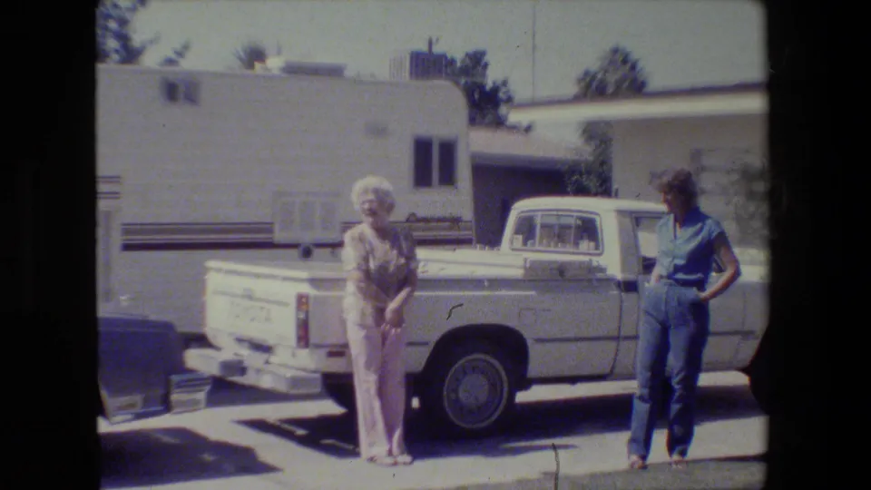 In 1984 San Francisco home-movie footage, two older women stand near a white Toyota pickup with a light-colored building behind them.