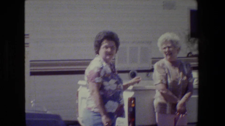Two older women in casual clothing appear to laugh and talk beside a white recreational vehicle in 1984 California home-movie footage.