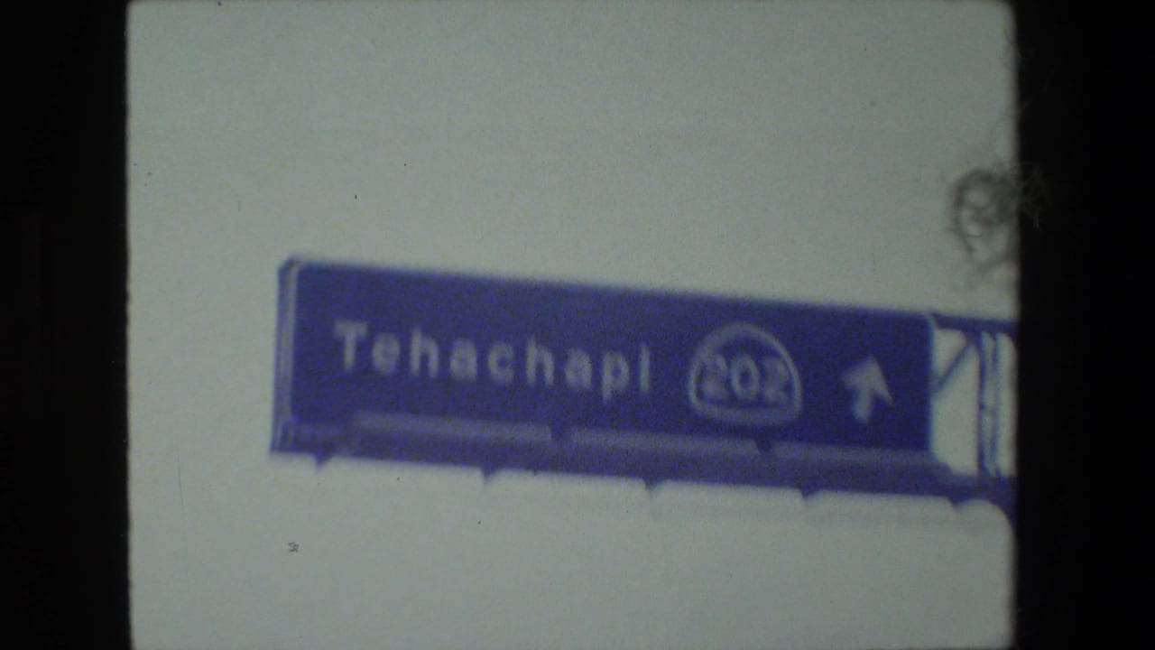 1984 8mm road-trip frame showing a blue Tehachapi highway sign viewed from inside a moving vehicle in California.
