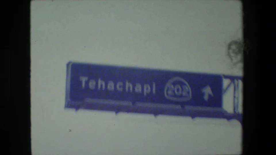 1984 8mm road-trip frame showing a blue Tehachapi highway sign viewed from inside a moving vehicle in California.