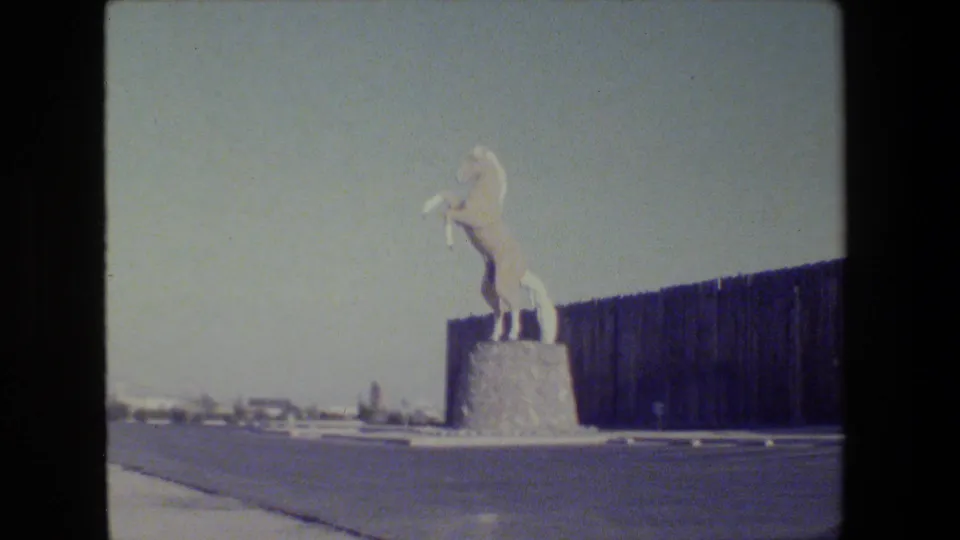 1984 California home-movie frame showing a white rearing horse statue on a stone pedestal near the museum exterior.