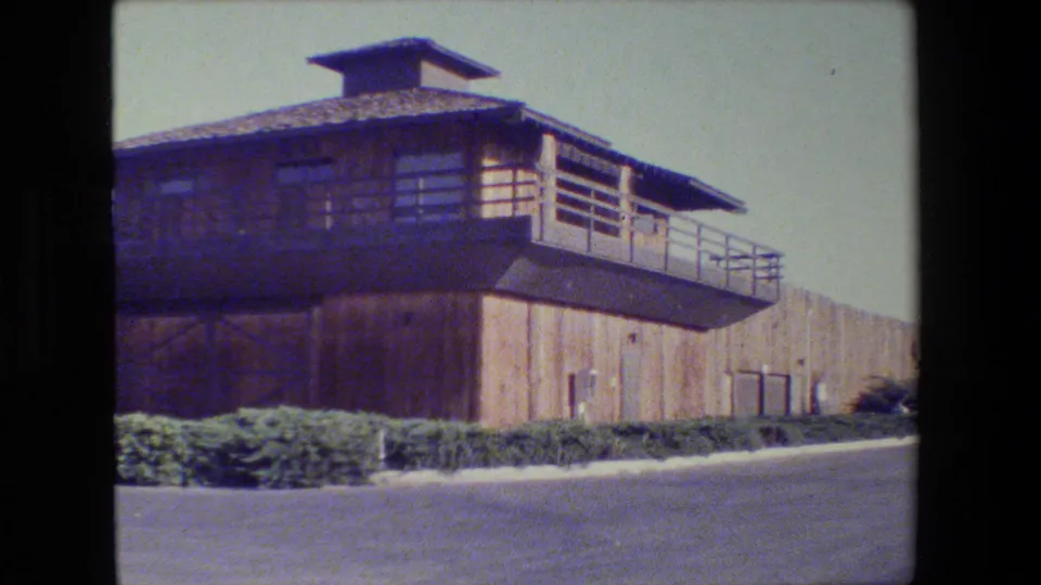 1984 San Francisco 8mm frame with the wood-sided structure closer in view, showing balcony rails, windows, shrubs, and paved foreground.