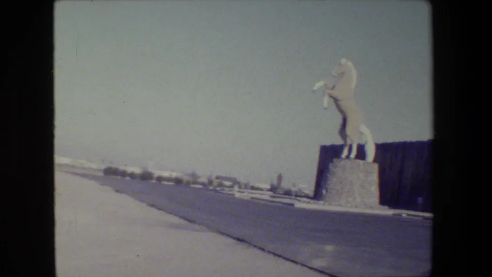 1984 San Francisco 8mm frame showing a white rearing horse statue on a stone pedestal beside a roadway and dark fence.