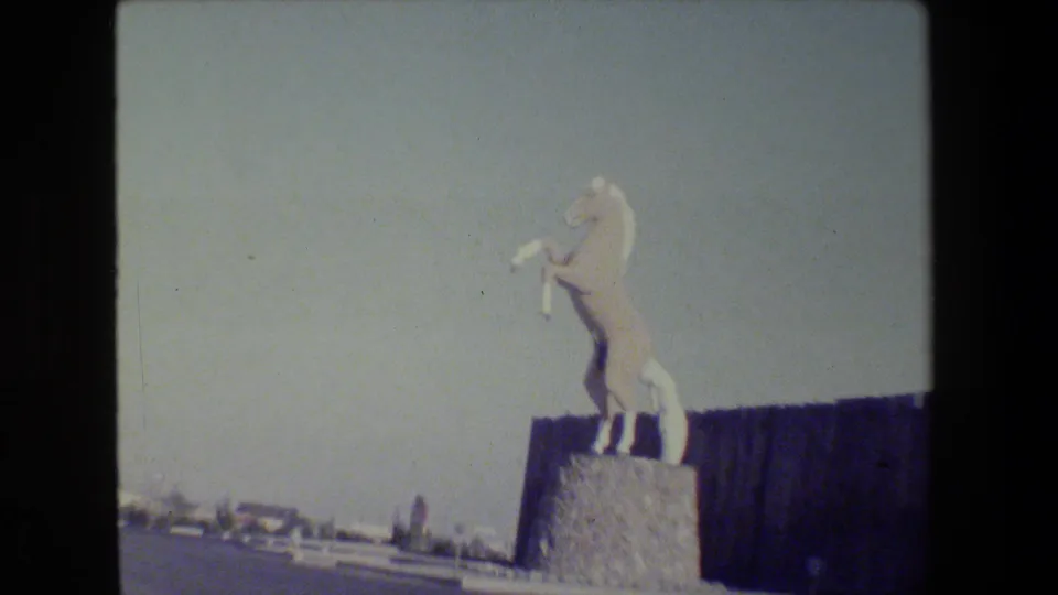 1984 San Francisco home-movie frame of the rearing white horse sculpture seen from a moving roadside viewpoint.