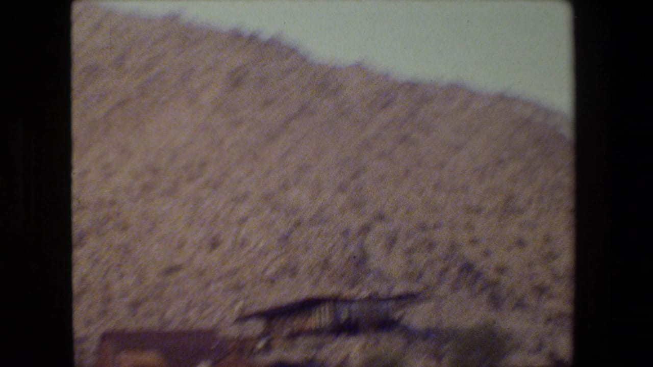 Rocky hillside seen from a moving vehicle, with a low structure partly visible near the bottom edge.
