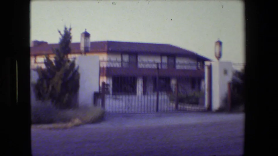 End frame of the gated driveway facing a two-story residential building with white pillars and wrought iron fencing.
