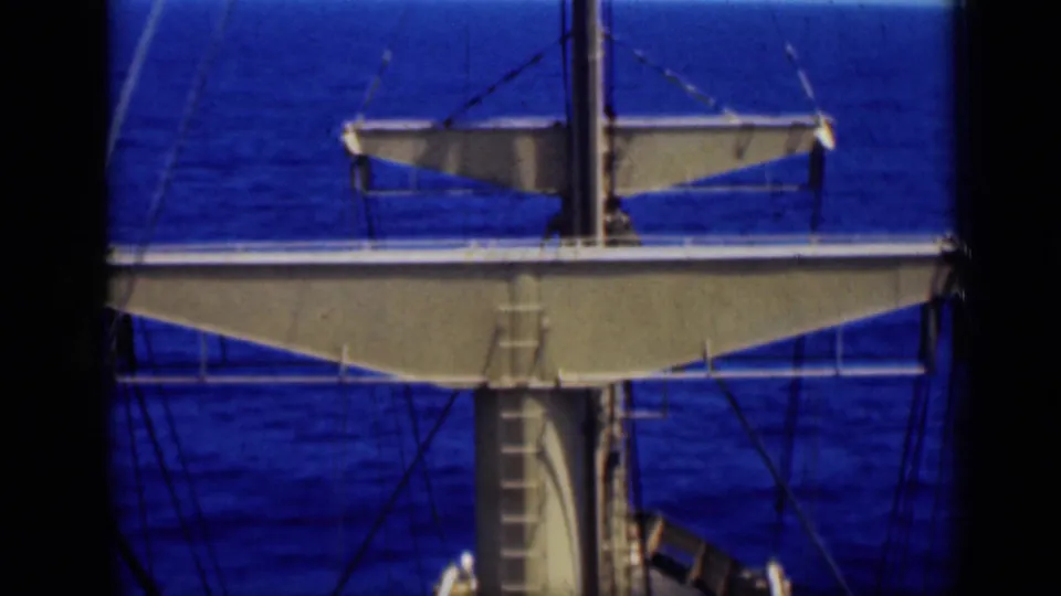 Shipboard 8mm frame with a mast, railings, rigging lines, and deck structure set against deep blue open water.