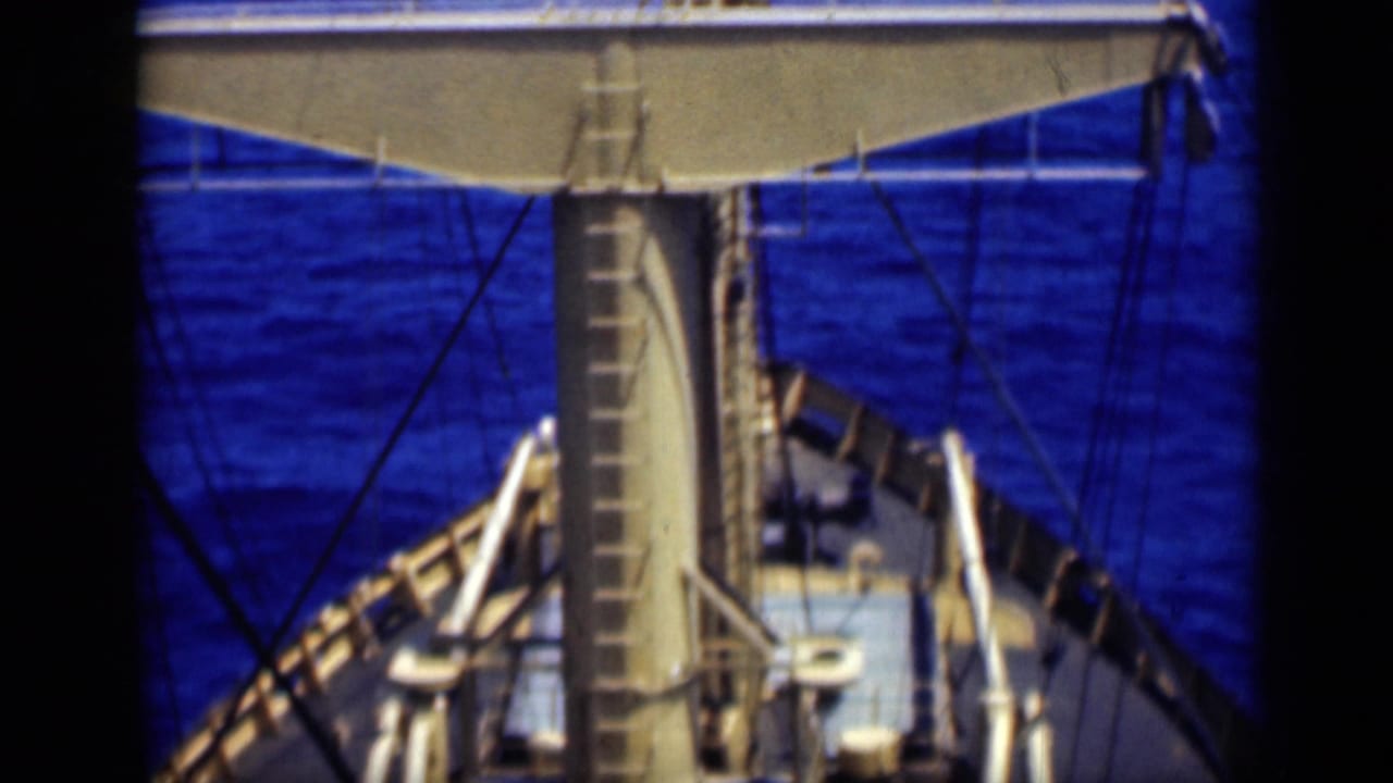 1946 8mm shipboard view from above the deck, showing a mast, ladder, rigging lines, railings, and blue ocean water.