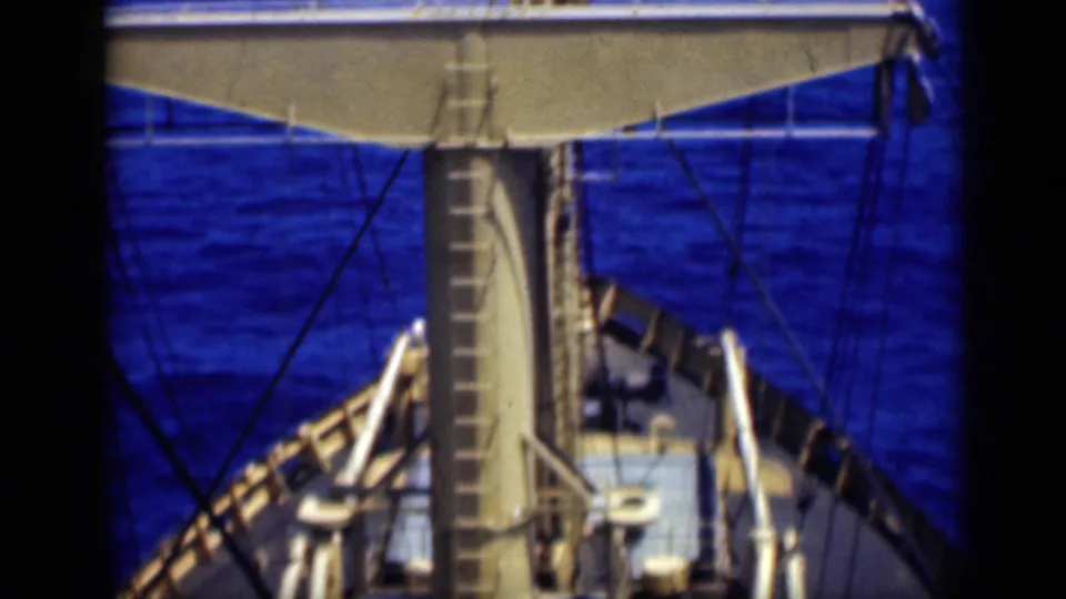 1946 8mm shipboard view from above the deck, showing a mast, ladder, rigging lines, railings, and blue ocean water.