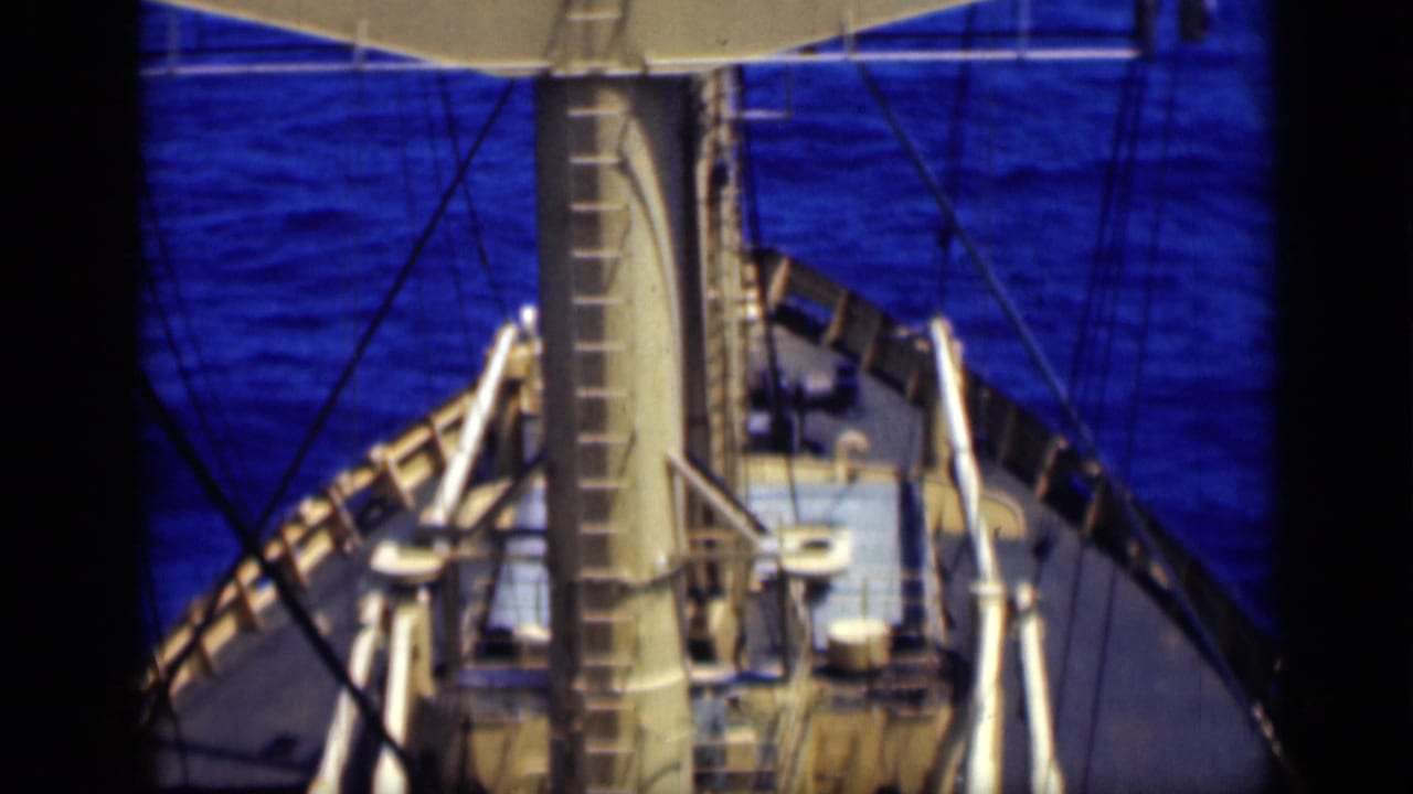 Elevated 1946 shipboard frame showing the mast centered above the deck, with rigging, railings, fittings, and blue water beyond.