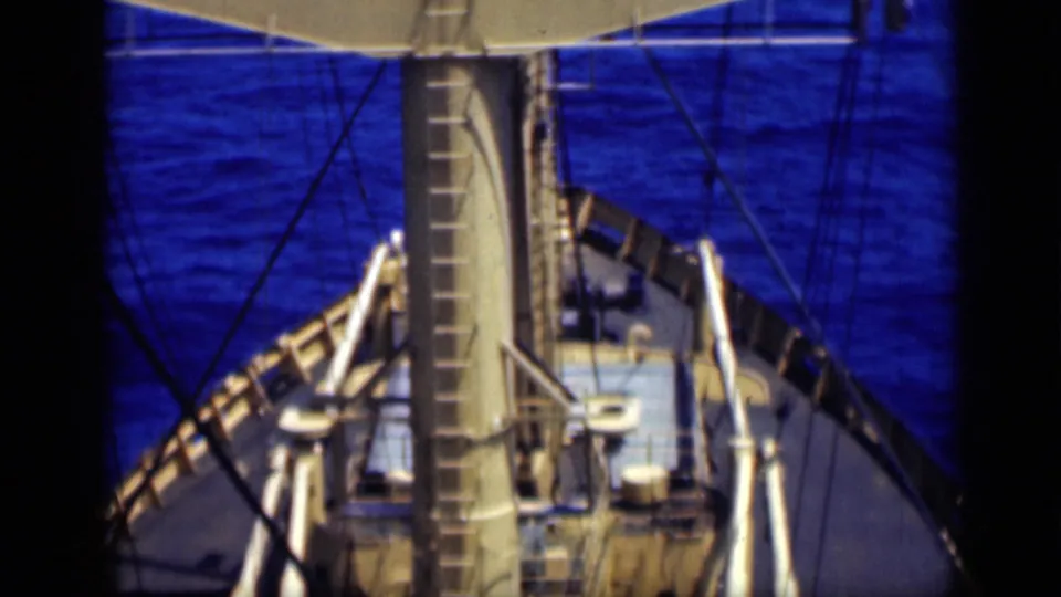 Elevated 1946 shipboard frame showing the mast centered above the deck, with rigging, railings, fittings, and blue water beyond.
