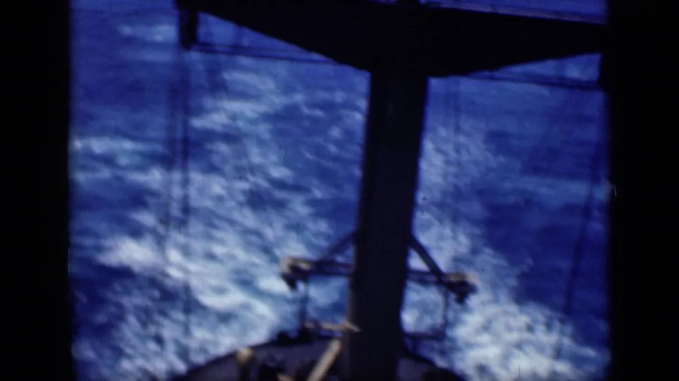 1946 8mm home-movie view over the ship's stern area, with dark framing, mast structure, rigging, and choppy wake.