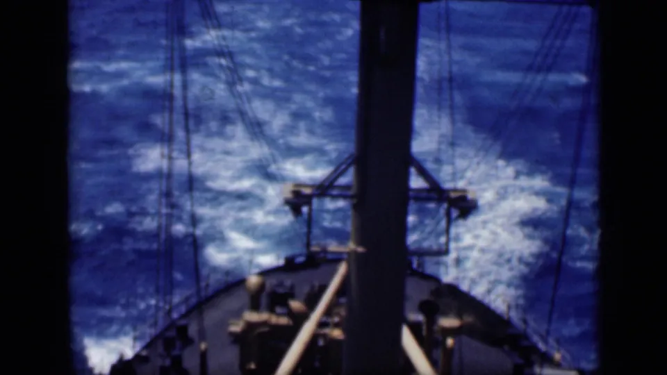 1946 8mm frame looking past a mast and rigging toward bright blue choppy water and the vessel's wake.