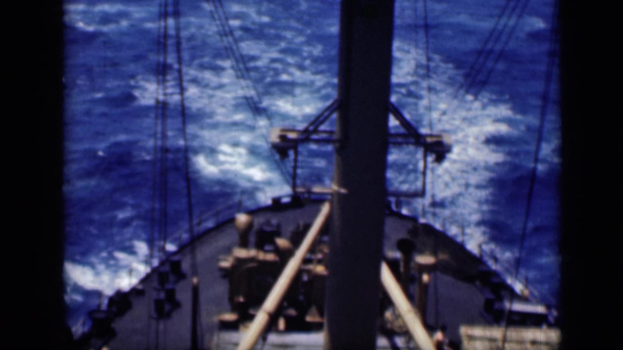 Bow of a vessel cutting through blue water with mast and rigging in view.