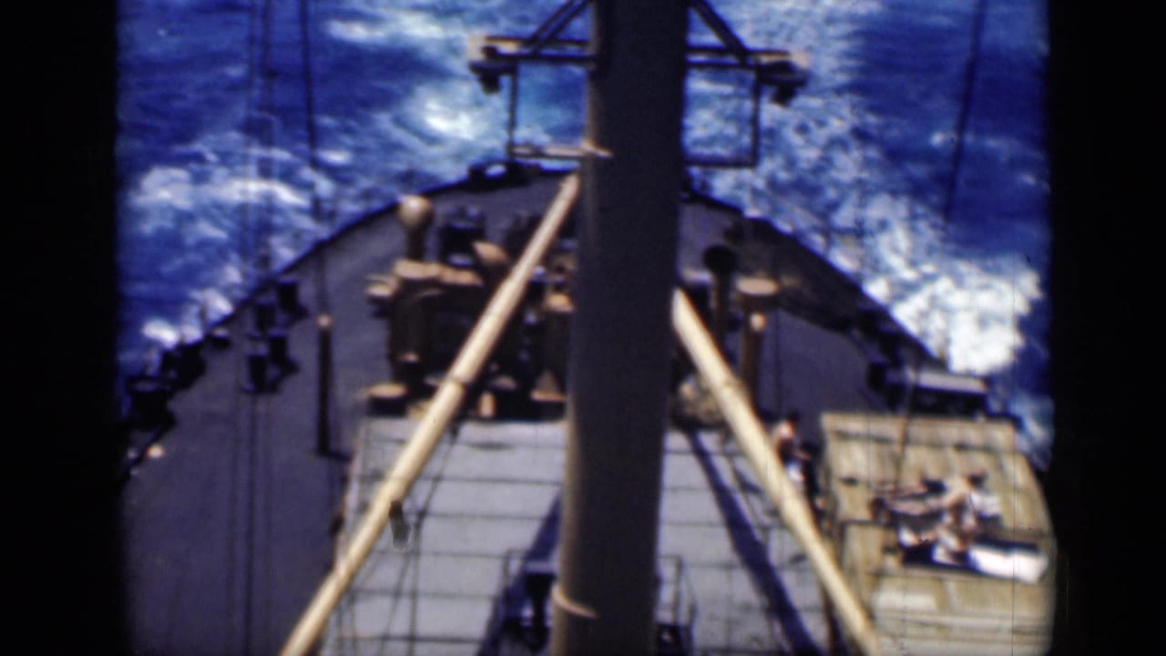 Ship deck seen from above with mast, rigging, blue water, and people on the right deck area.