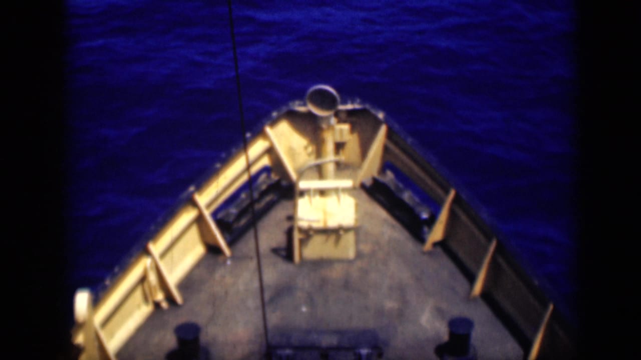 Ship bow and railings point into deep blue water, with deck fittings near the foreground.