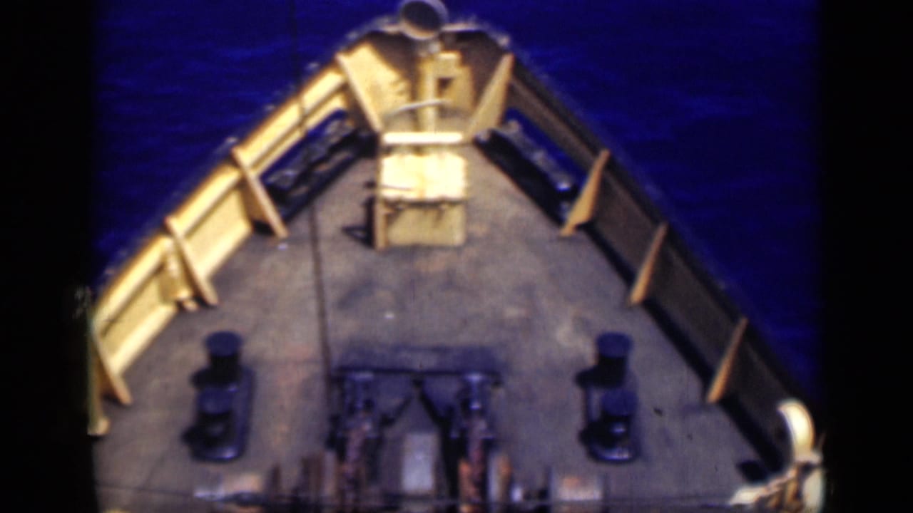 1946 Egypt 8mm frame showing a high-angle view over the bow of a fishing boat with pale railings, dark bollards, winch gear and deep blue water.