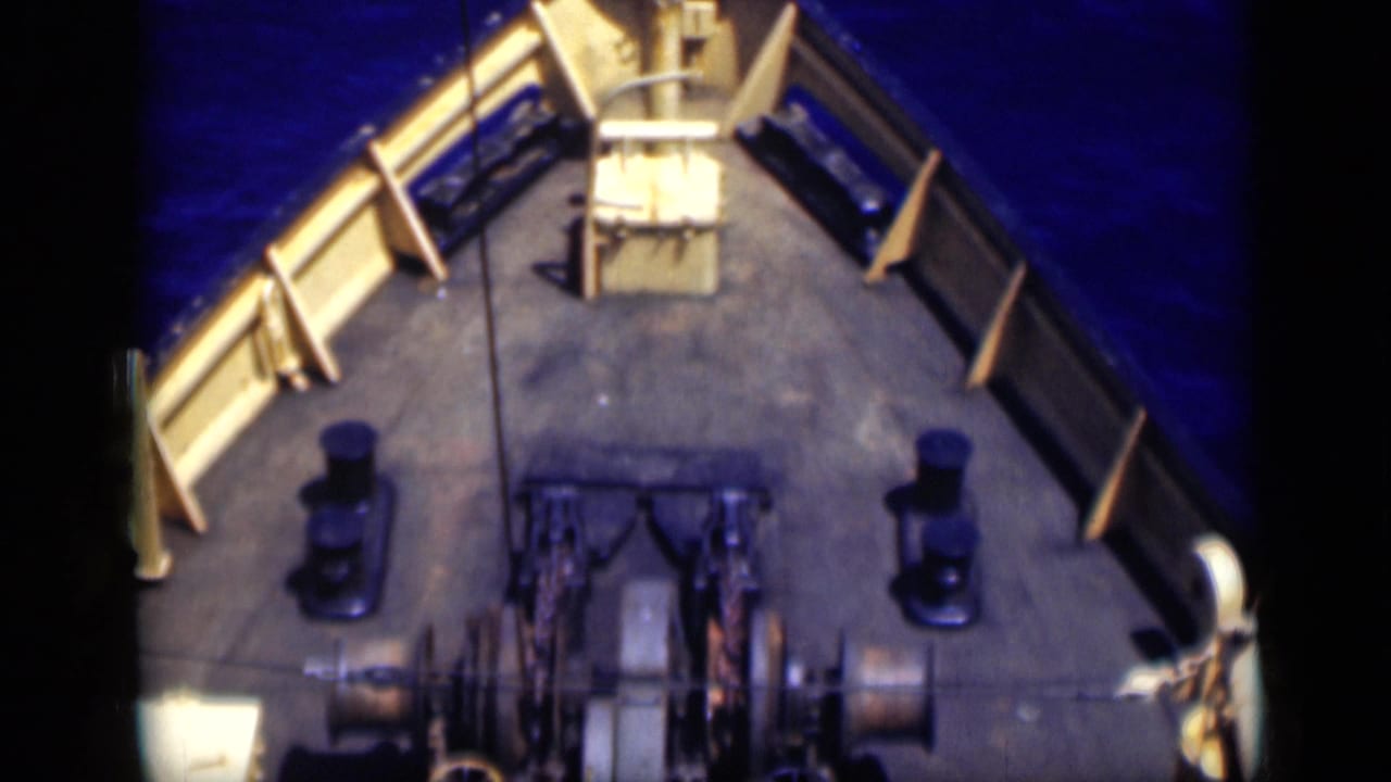 High-angle view of the boat bow with railings, bollards and machinery over blue water.