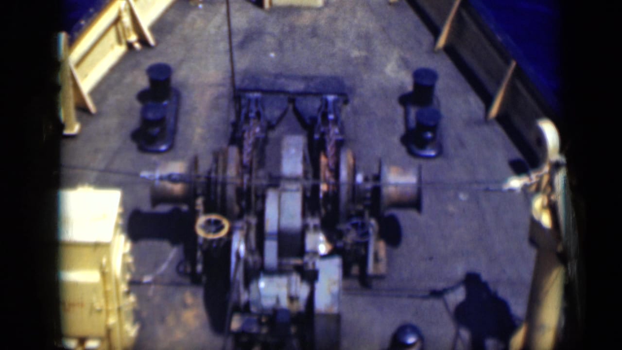 1946 Egypt 8mm frame showing the fishing boat's deck machinery, cable or net spools, bow railings and surrounding blue water from a high onboard angle.