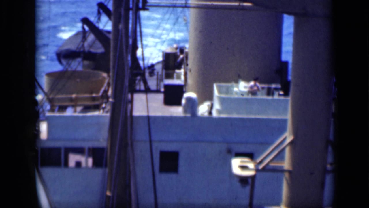 Ship deck and funnel with railings, rigging, deck equipment, and ocean in the background.