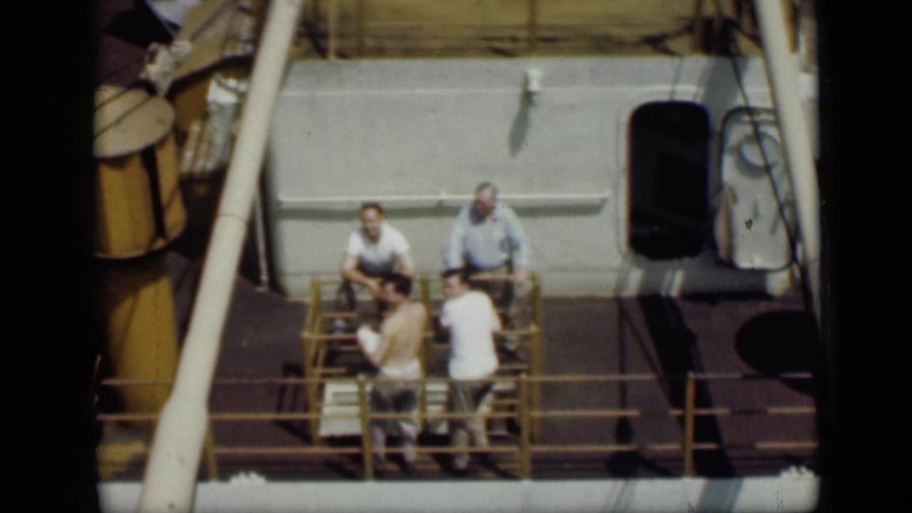 1946 Cairo 8mm footage showing four men in light clothing gathered on a boat deck beside yellow railings and cabin structures.